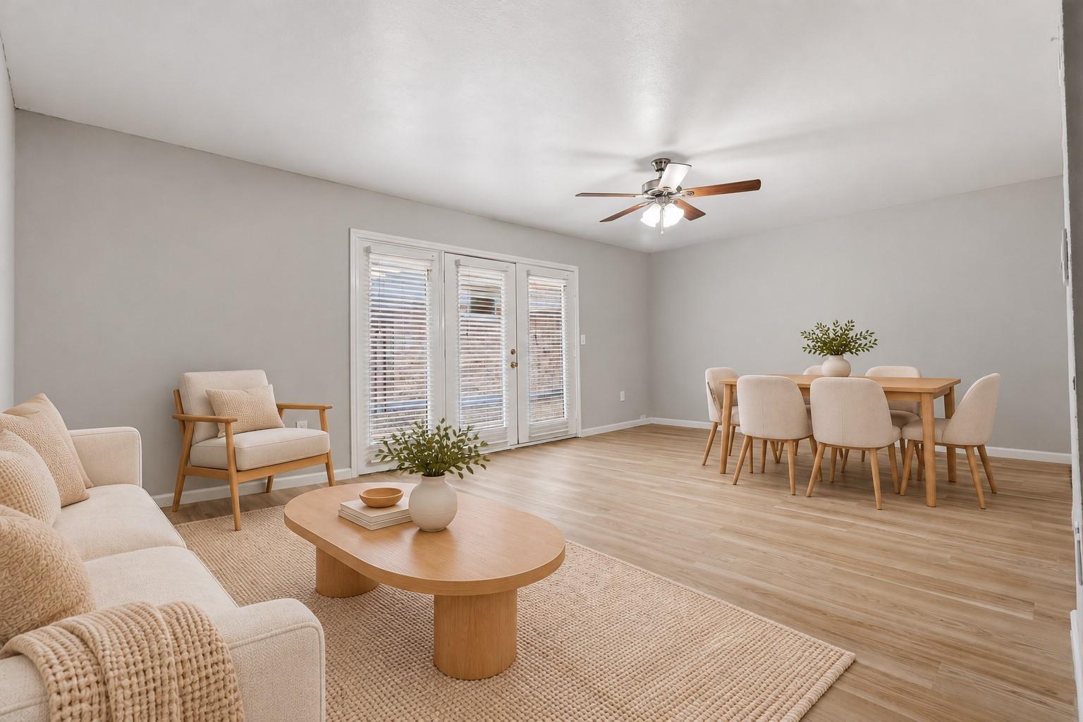 Open-plan living and dining room with French doors, a cream sofa, and a wooden dining table.