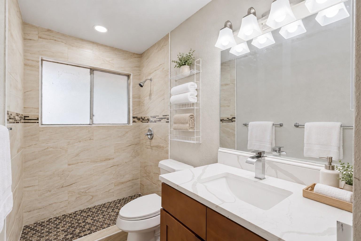 Bathroom with beige tile shower, hexagonal mosaic floor, and white sink on a wood vanity.