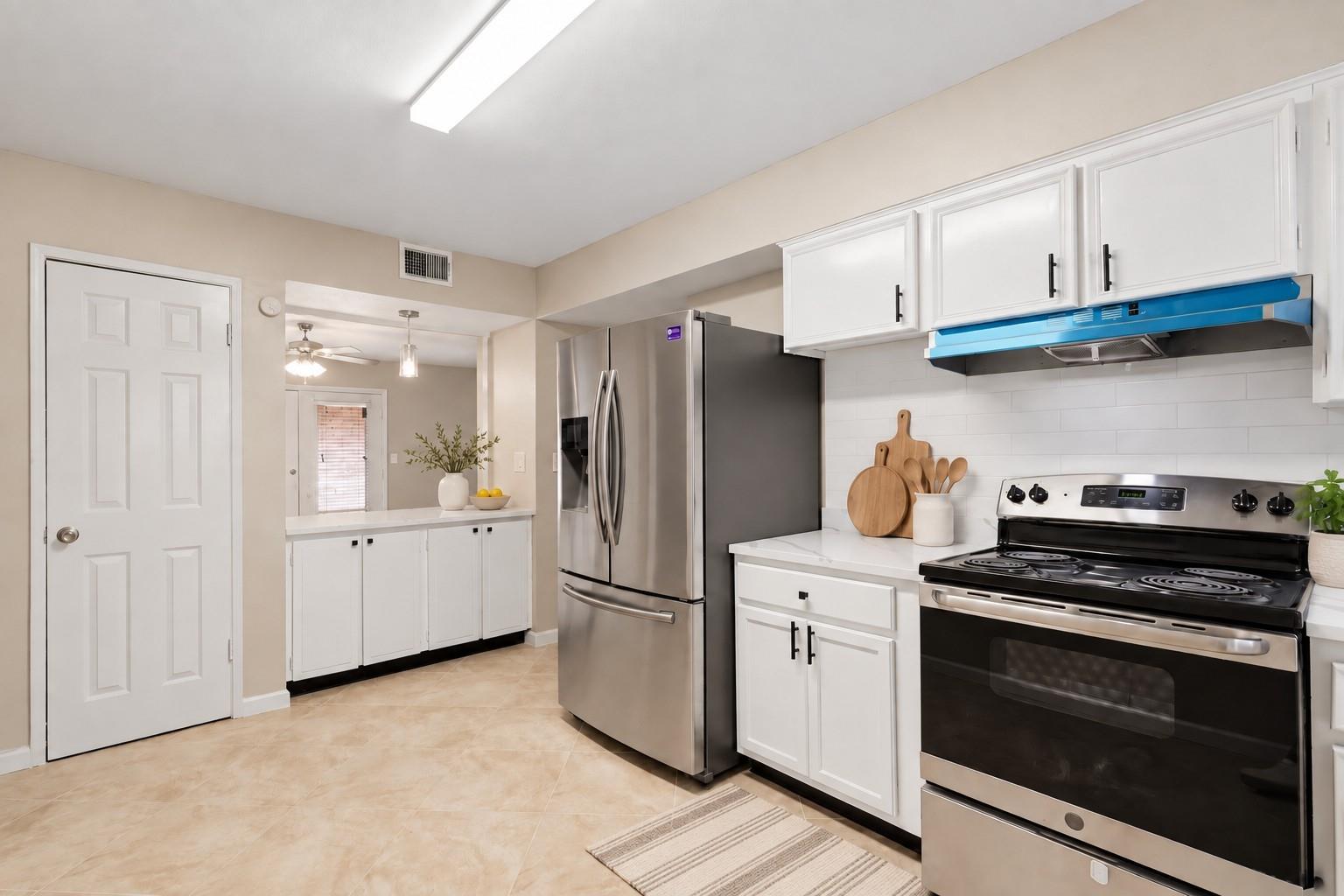 Kitchen with white cabinets, stainless appliances, and a blue range hood.