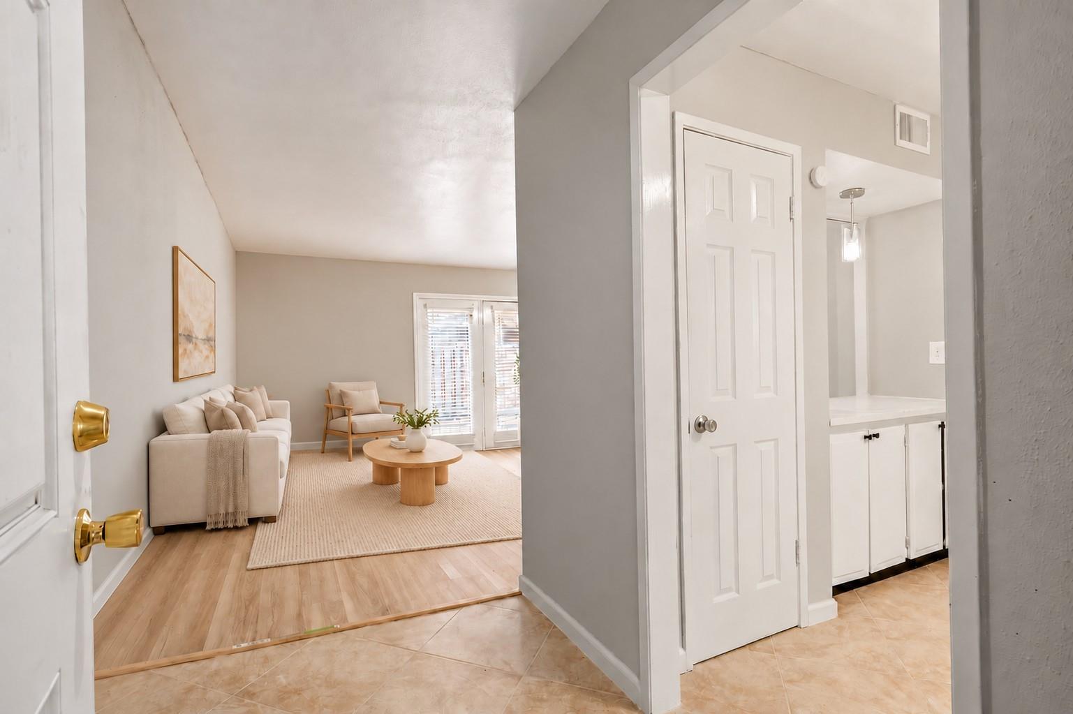 Living room with neutral seating, a round wood coffee table, and glass doors with blinds.