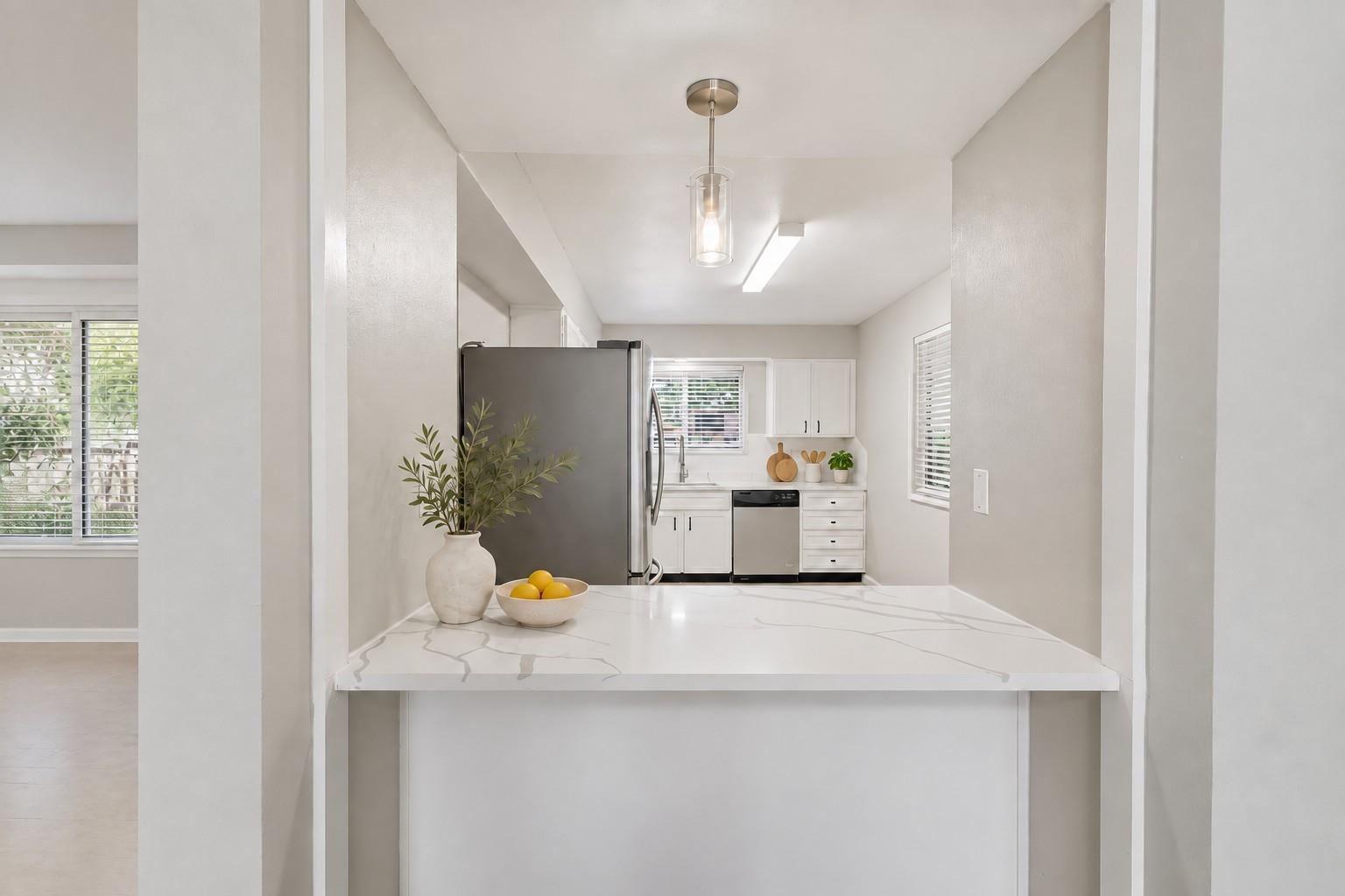 Bright kitchen with white cabinetry, stainless steel appliances, and a marble-look peninsula.