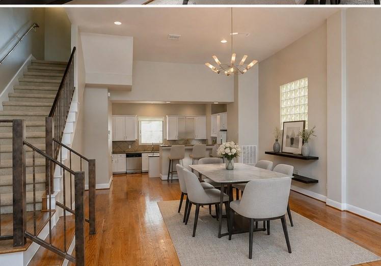 Open-plan dining room with a long table, upholstered chairs, hardwood floors, and an adjacent kitchen.
