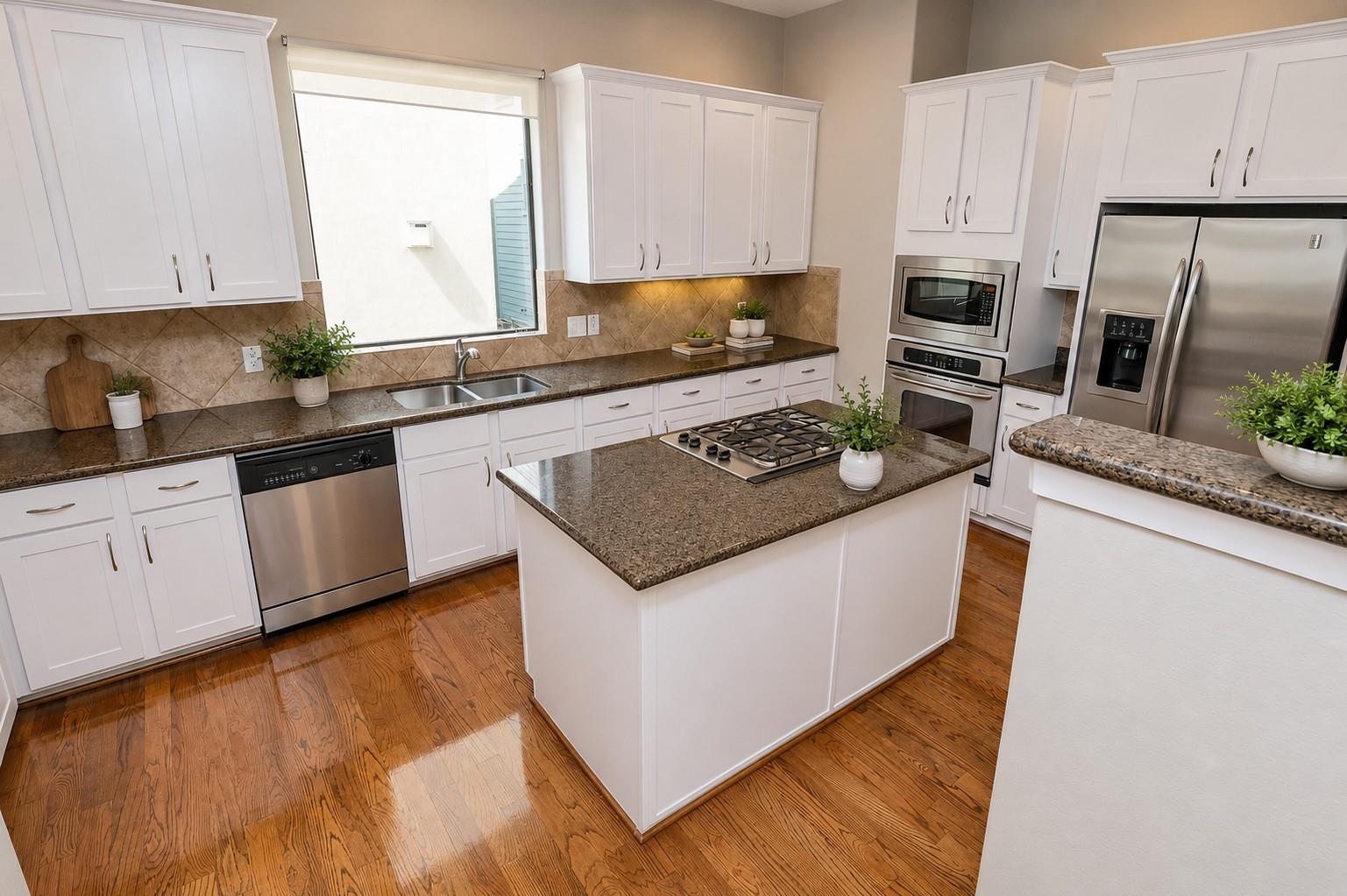 Kitchen with white cabinets, granite island and gas cooktop, stainless appliances, and hardwood floors.