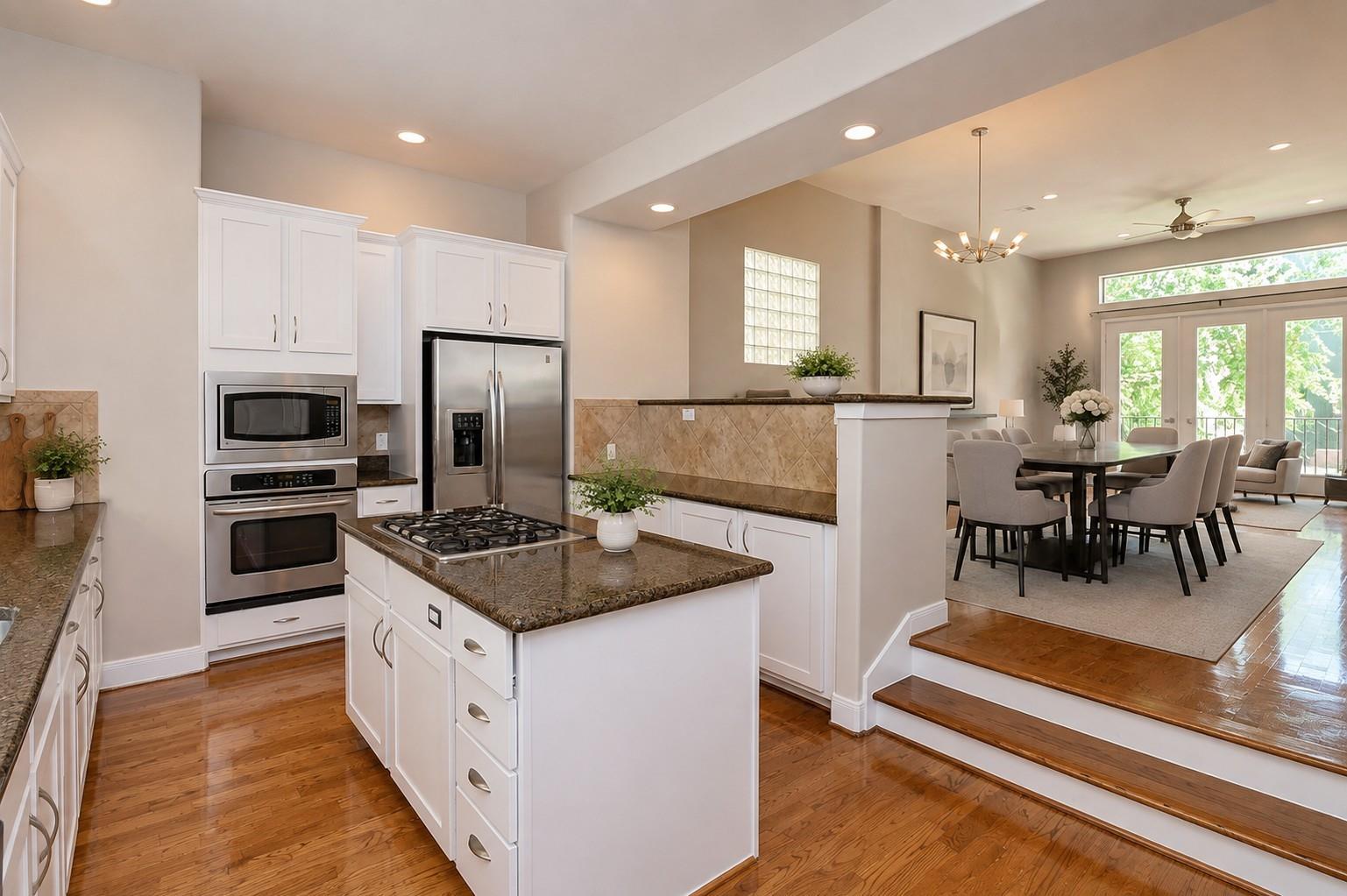 Open-plan kitchen with a granite island and gas cooktop beside a dining area with glass balcony doors.