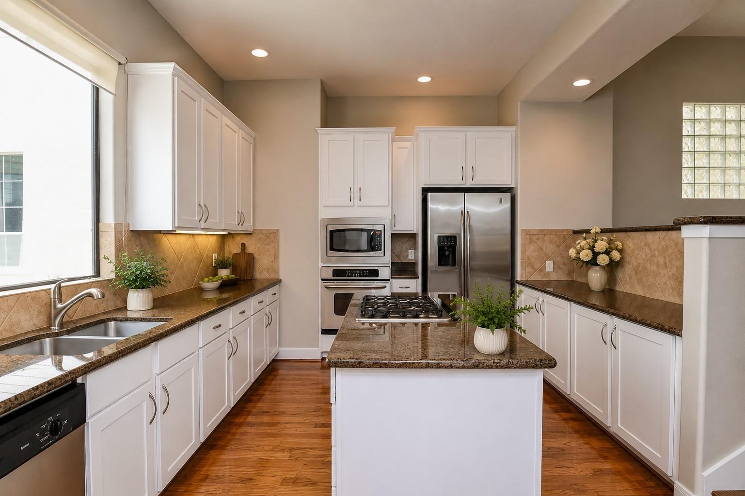 Kitchen with white cabinets, granite counters, a large cooktop island, and stainless steel appliances.