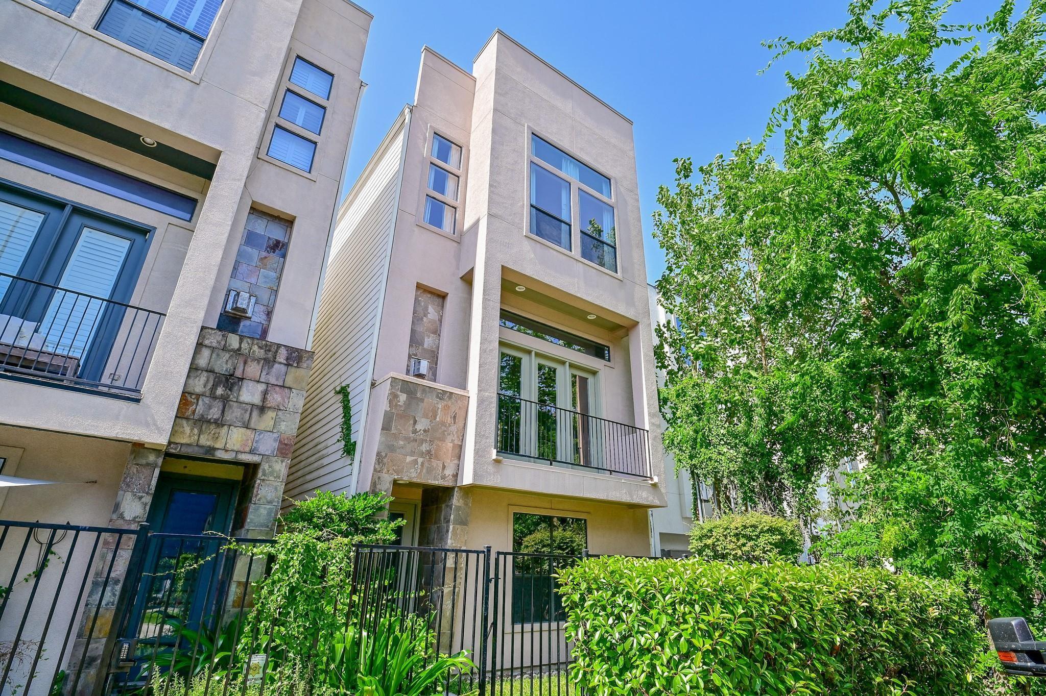 Modern townhouse exterior with stone accents, balconies, and leafy trees.