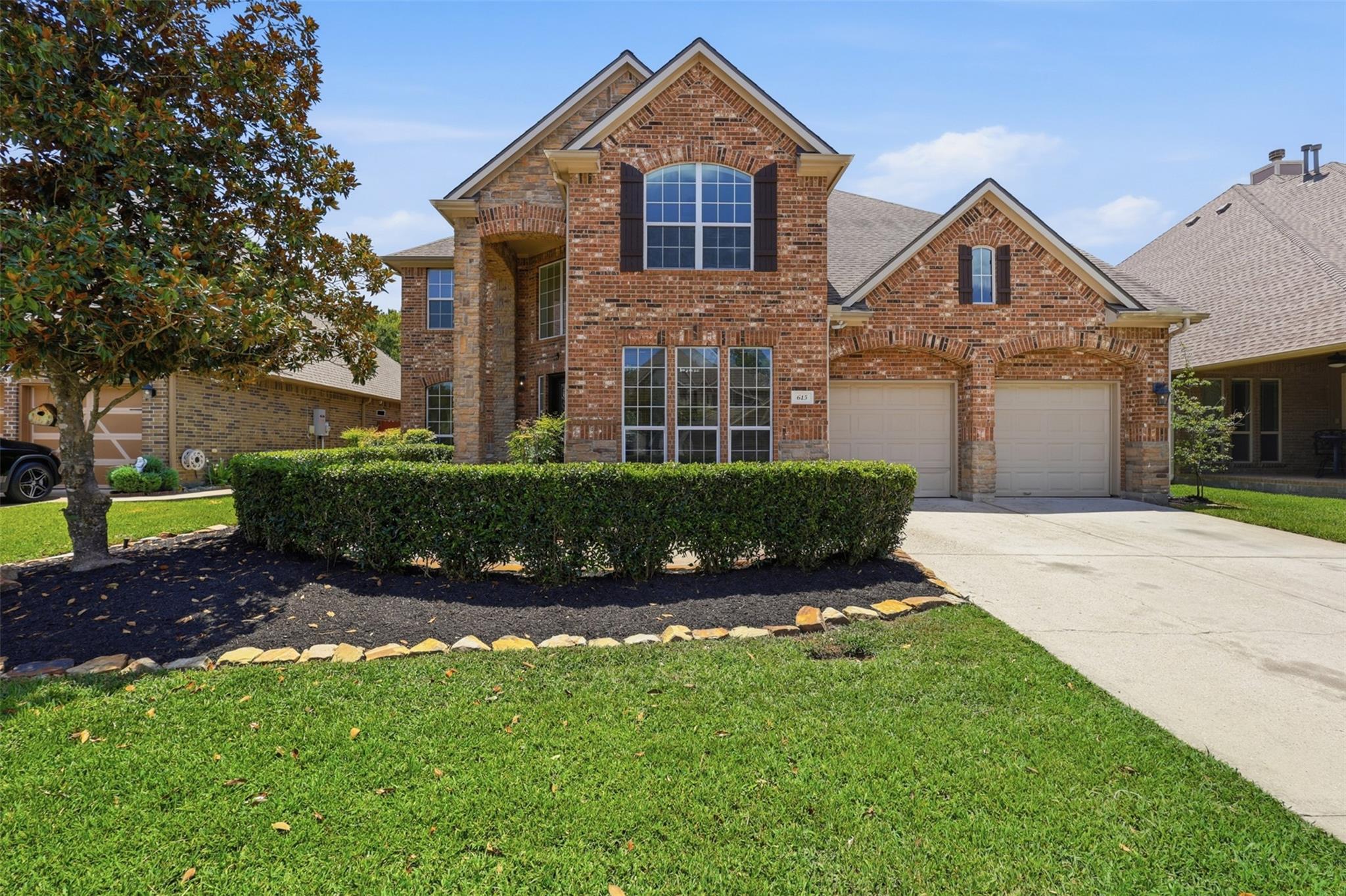 Two-story brick house with arched windows, a trimmed hedge, and a two-car garage.