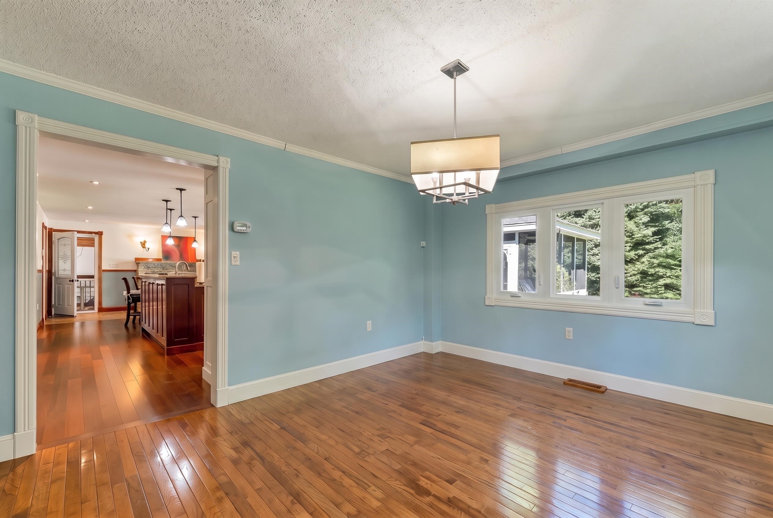 Empty blue dining room with polished hardwood floors, a chandelier, and a large window.