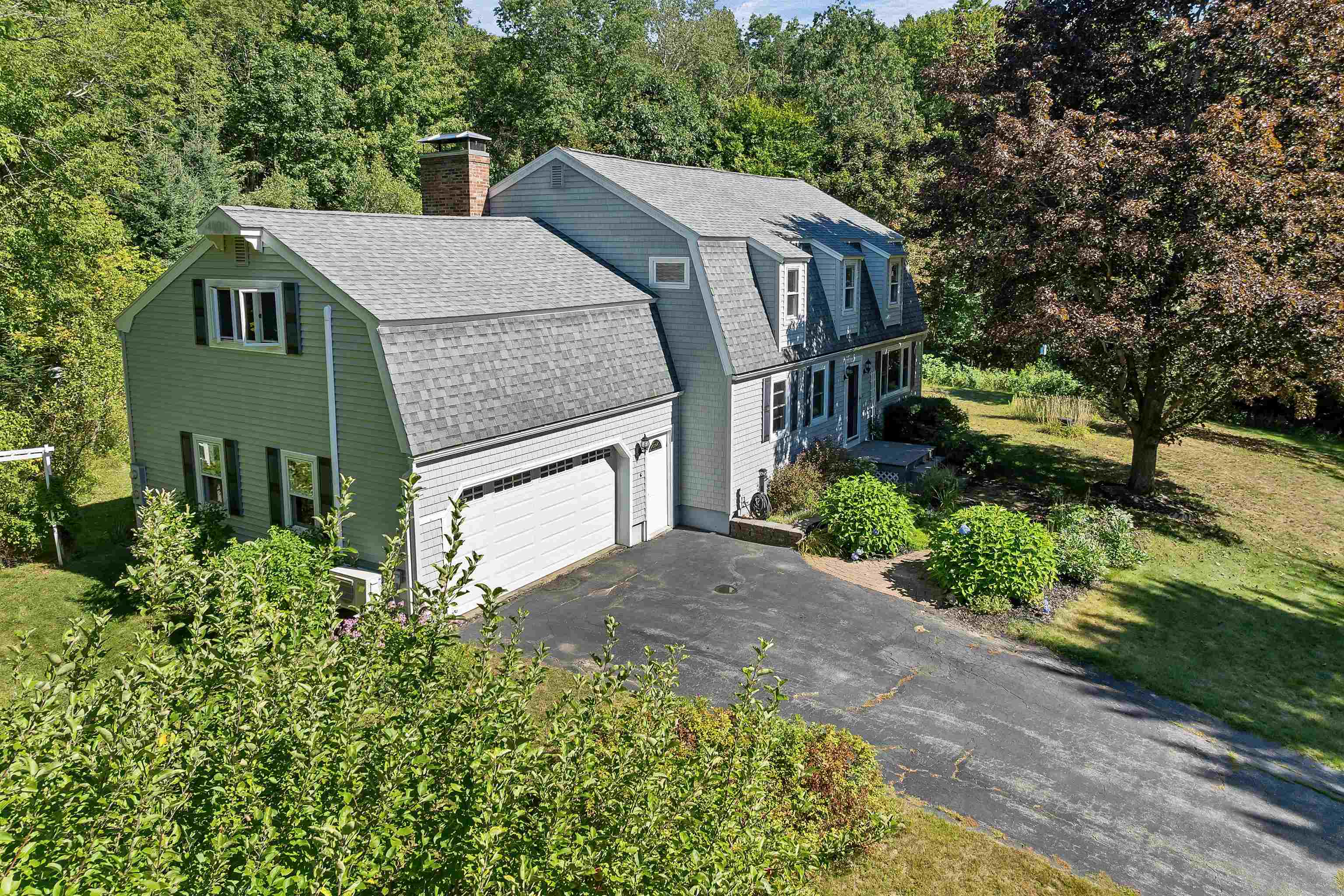 Gray-shingled two-story house with a double garage, broad driveway, and mature trees.