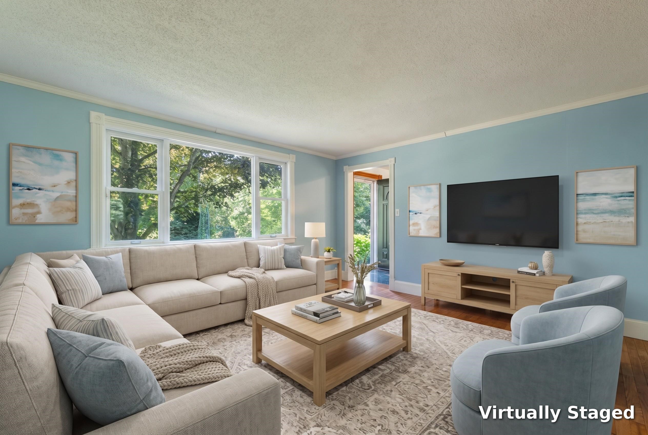 Virtually staged living room with a beige sectional, blue walls, and large windows overlooking trees.