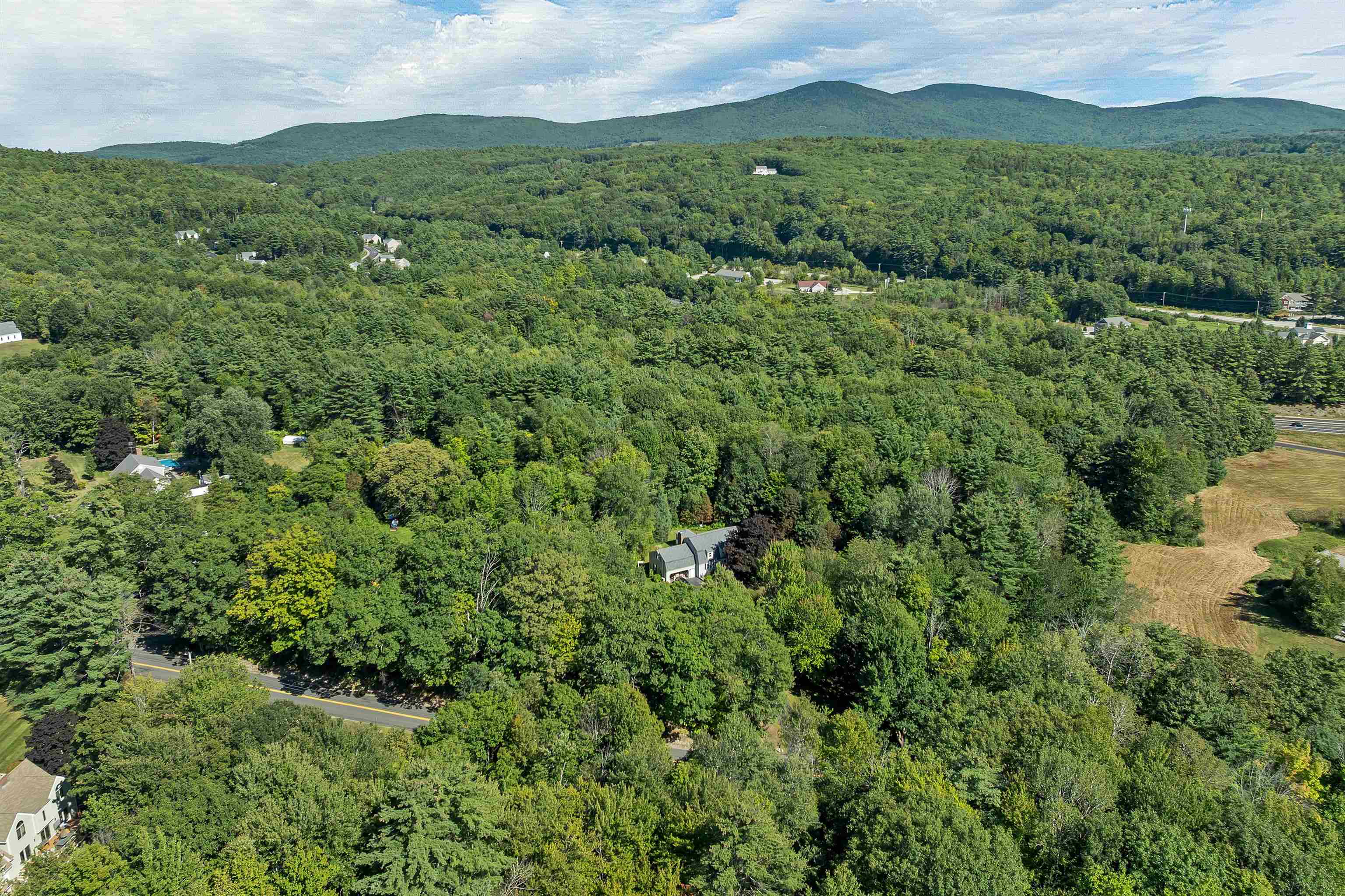 Aerial view of a wooded property with a house, road, and mountains beyond.