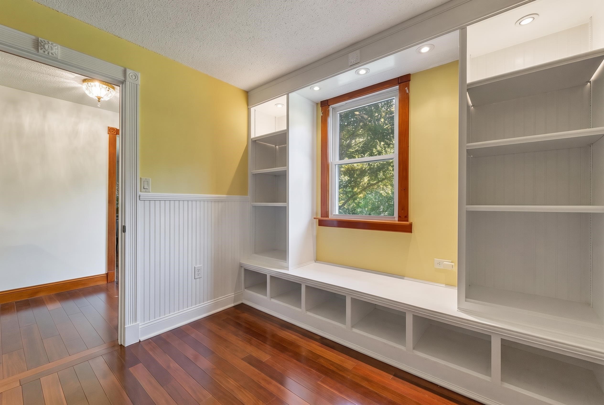 Interior room with built-in white shelves and window seat, yellow walls, and hardwood floors.