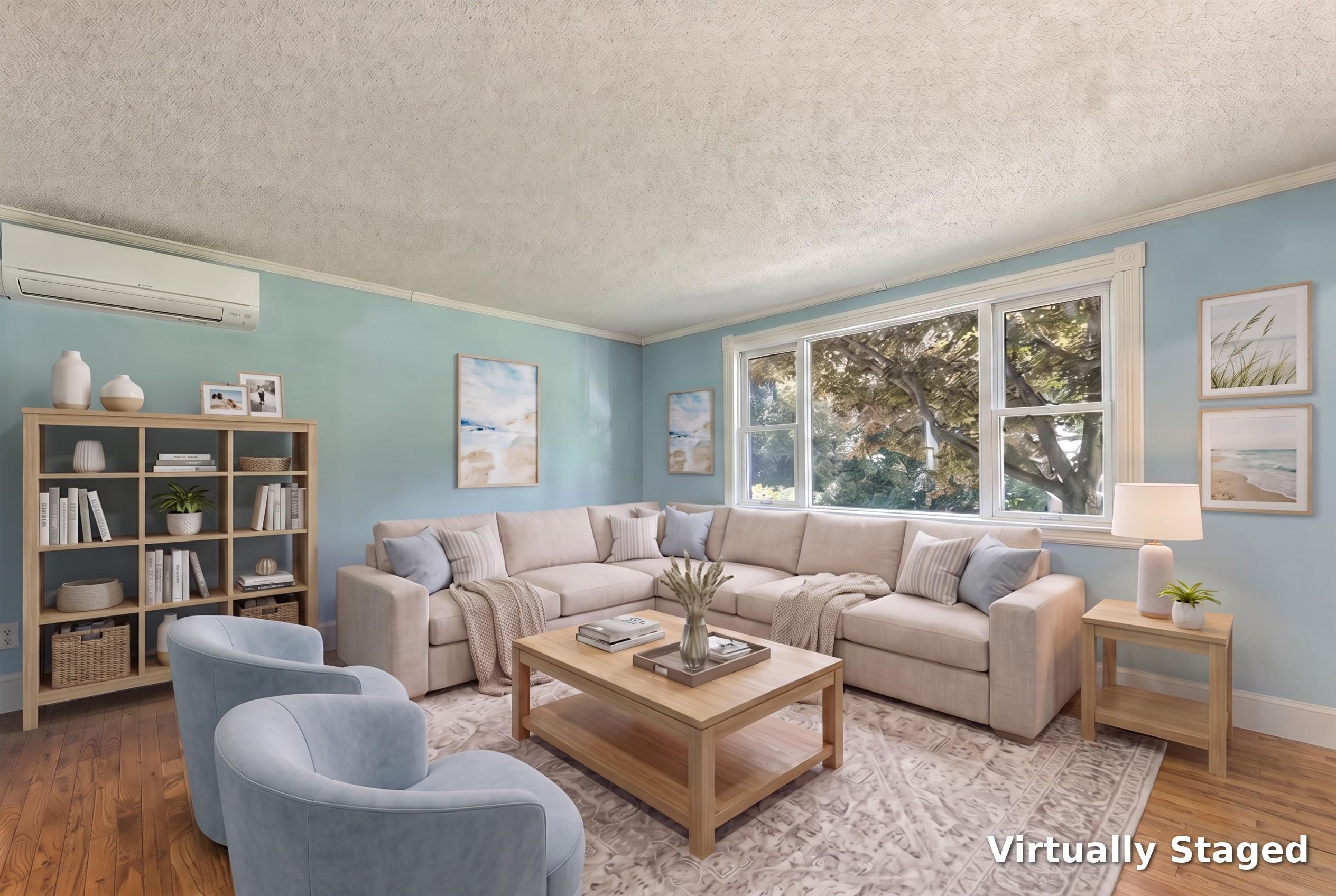 Virtually staged living room with a beige sectional, pale blue walls, and large windows overlooking trees.