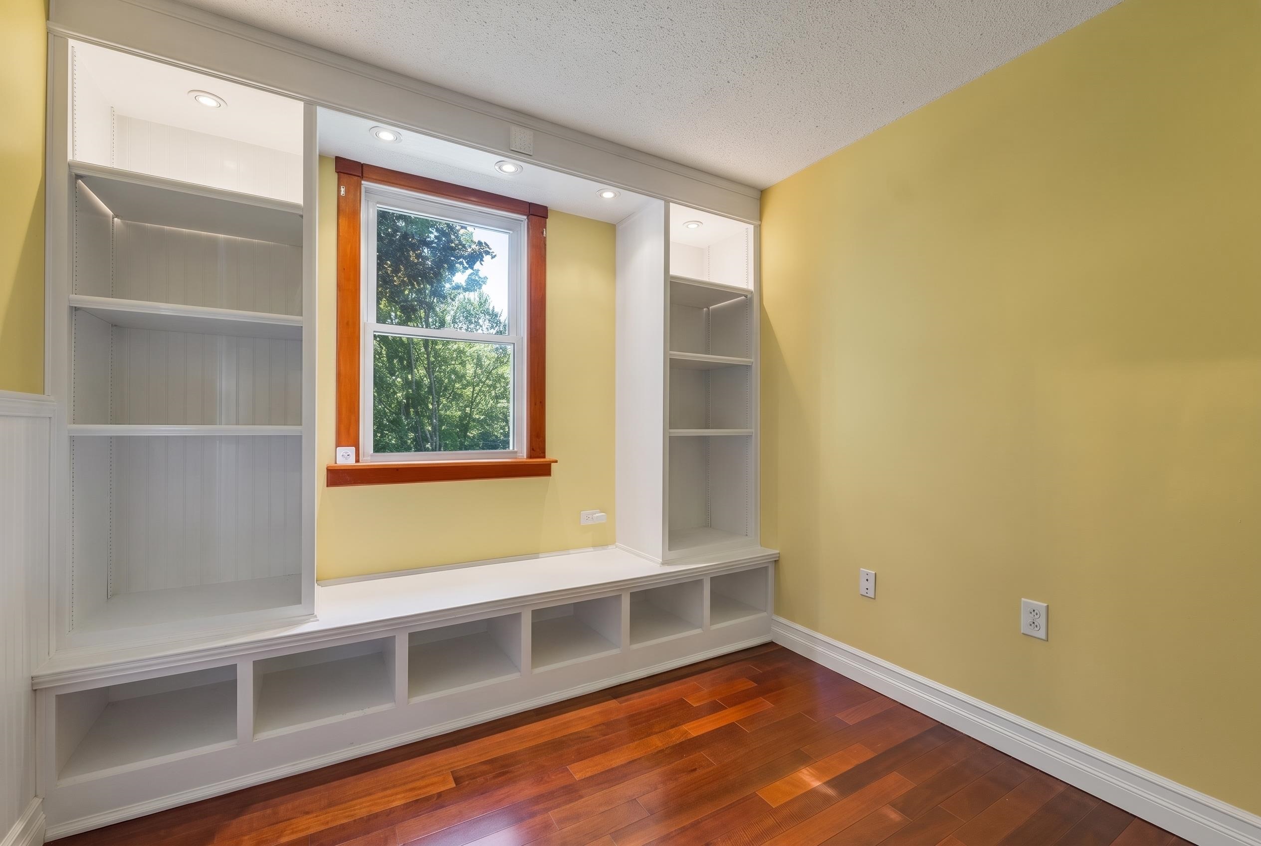 Empty room with built-in white shelves and bench seating around a wood-trimmed window.