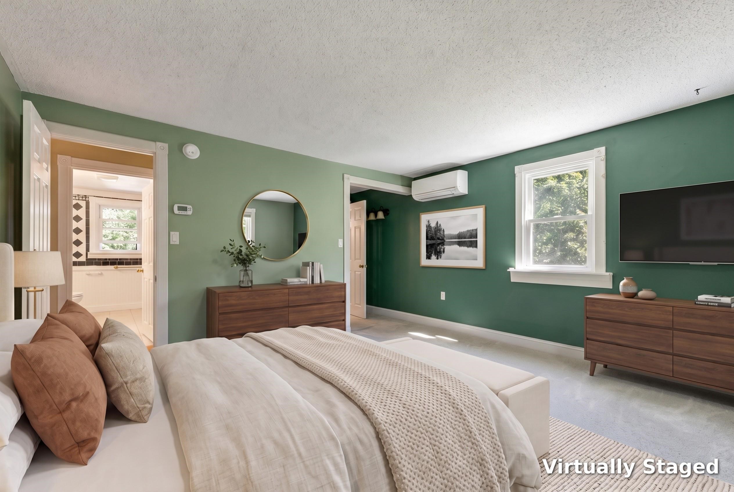 Bedroom with green walls, a large bed, wood dressers, and an adjoining bathroom.