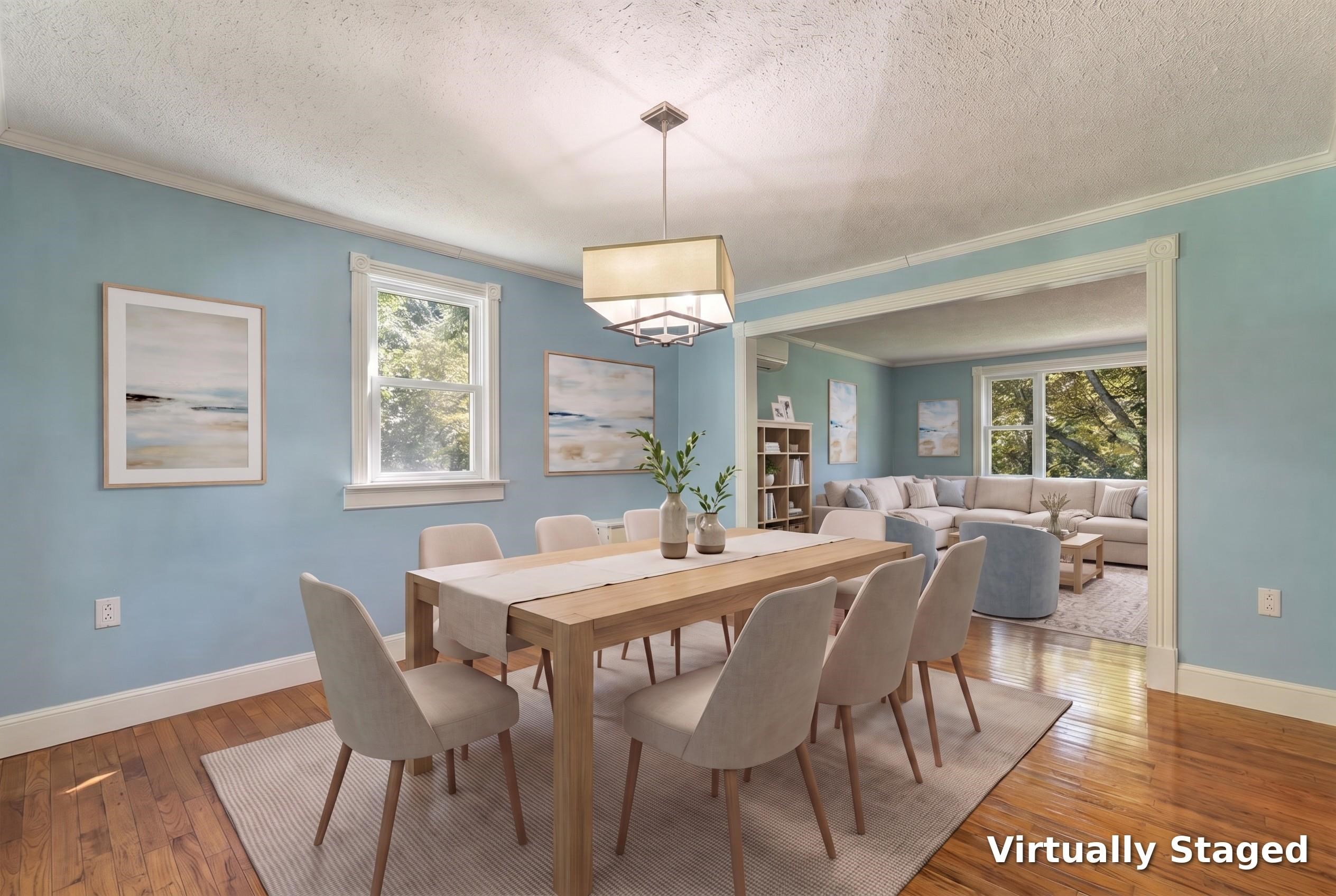 Virtually staged dining room with a wood table, blue walls, and an adjoining living room with large windows.