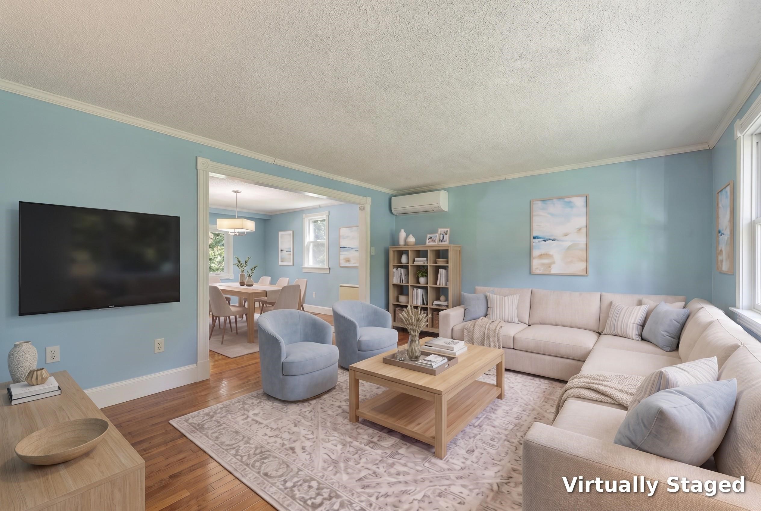 Virtually staged living room with a cream sectional, blue armchairs, and an open dining area.