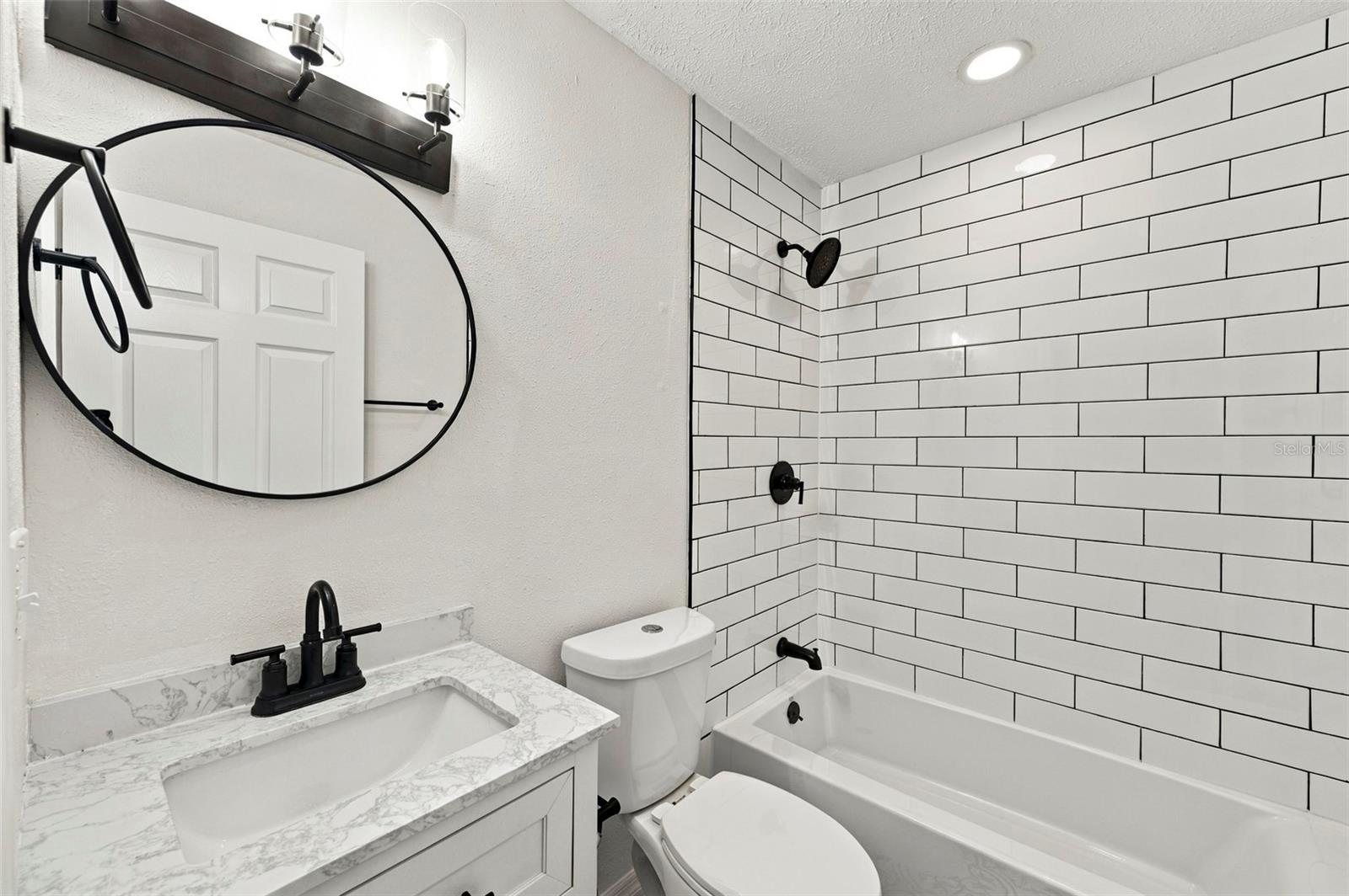 Bathroom with white subway-tile tub surround, black fixtures, and a marble-look vanity.