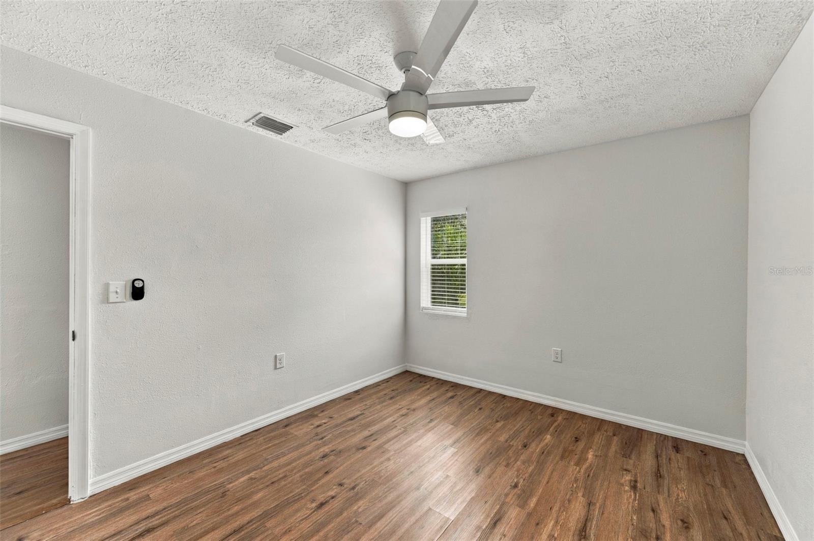 Empty room with wood-look flooring, a ceiling fan, and a small window with blinds.