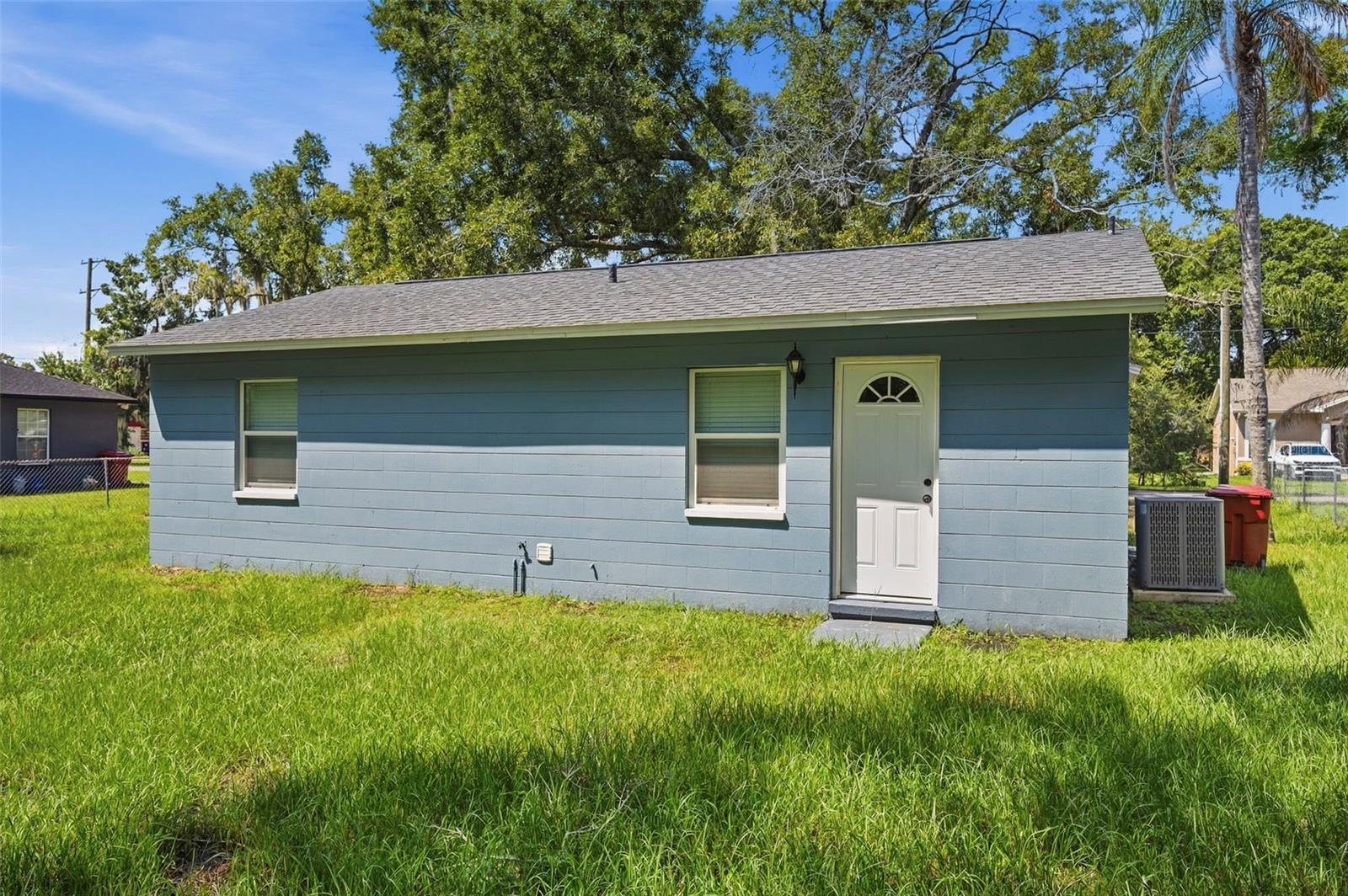 Small blue house with a white front door, two windows, and a grassy yard.