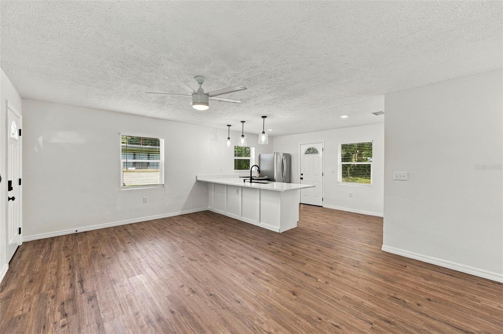 Open kitchen with a large white island, stainless steel refrigerator, and wood-look flooring.