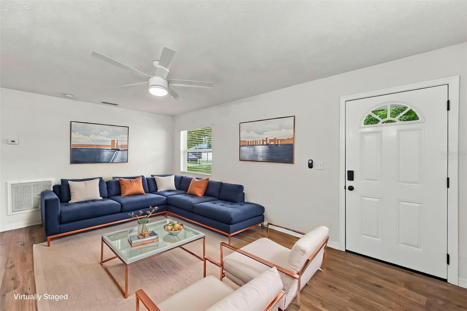 Virtually staged living room with a navy sectional, pale chairs, and glass coffee table.