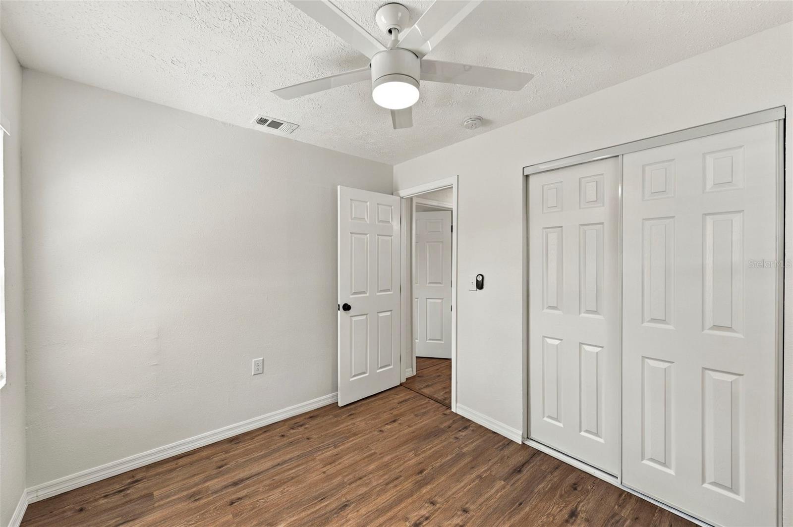 Empty bedroom with a ceiling fan, wood-look flooring, and a large sliding-door closet.