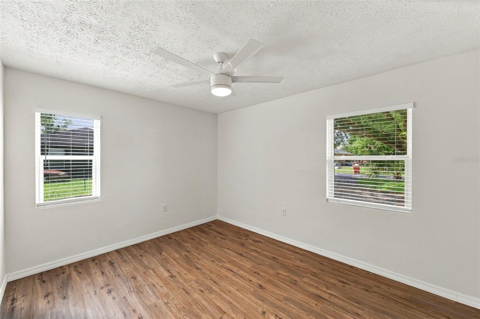 Empty room with wood-look floors, two windows with blinds, and a ceiling fan.