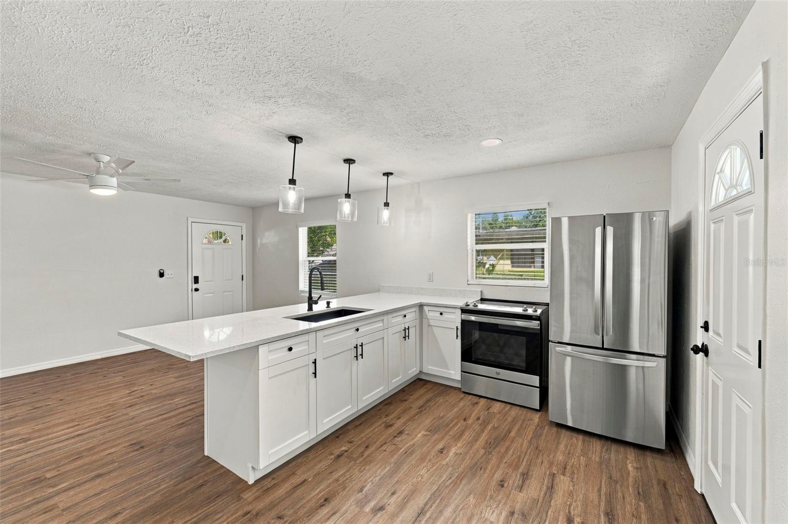 Open-plan kitchen with a white island, stainless steel appliances, and wood-look flooring.