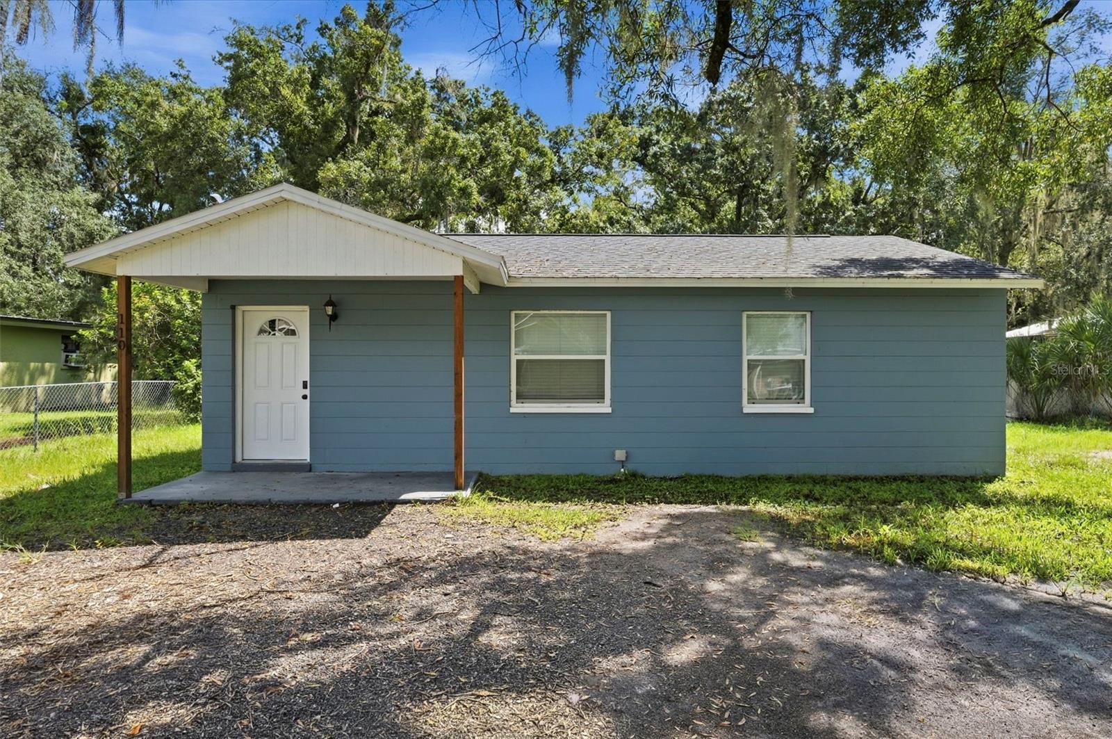 Blue single-story house with a white covered porch and mature trees.