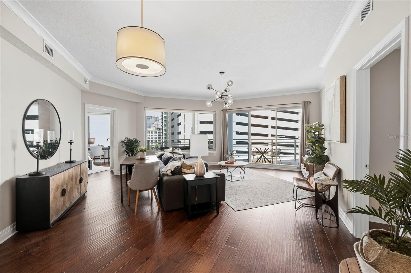 Furnished condo living room with hardwood floors, large windows, and a balcony overlooking nearby buildings.