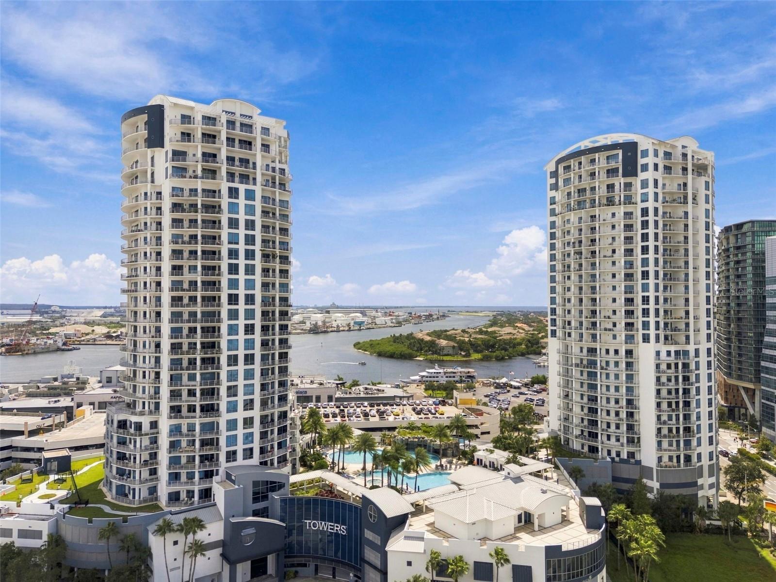 Two white condominium towers beside a Tampa waterway, with a pool and marina below.