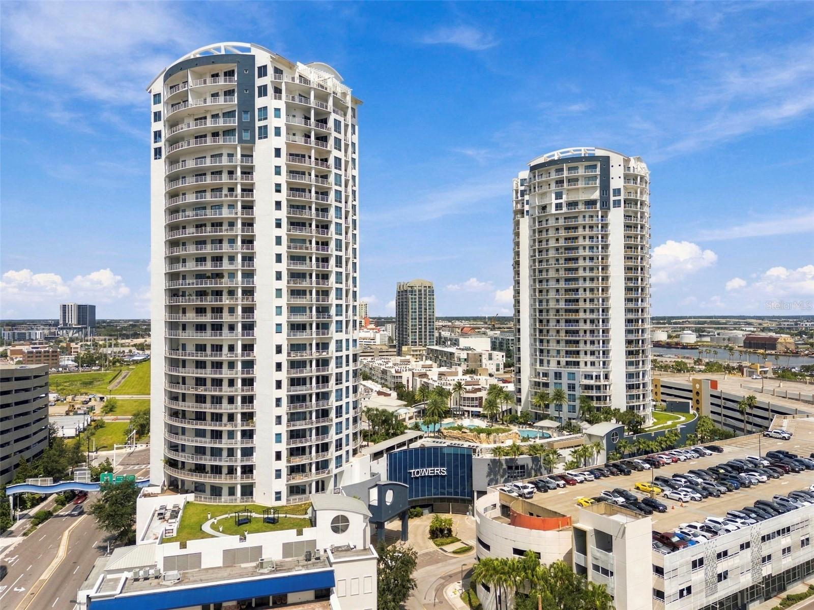 Two white high-rise condominium towers with curved balconies, a pool, and parking lots.
