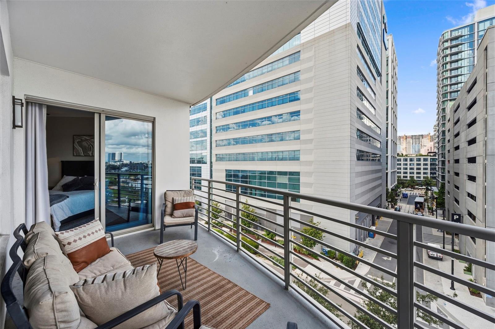 Furnished condo balcony with cushioned seating and a view of downtown buildings.