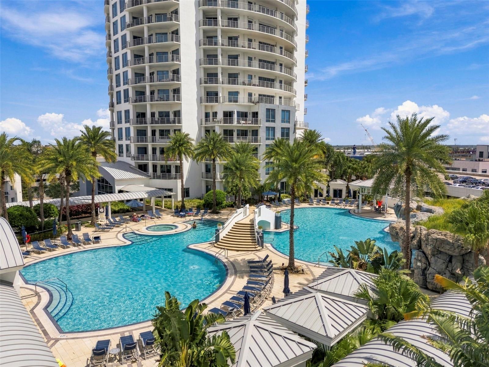 High-rise condominium overlooking a resort-style pool, spa, and palm-lined sun deck.