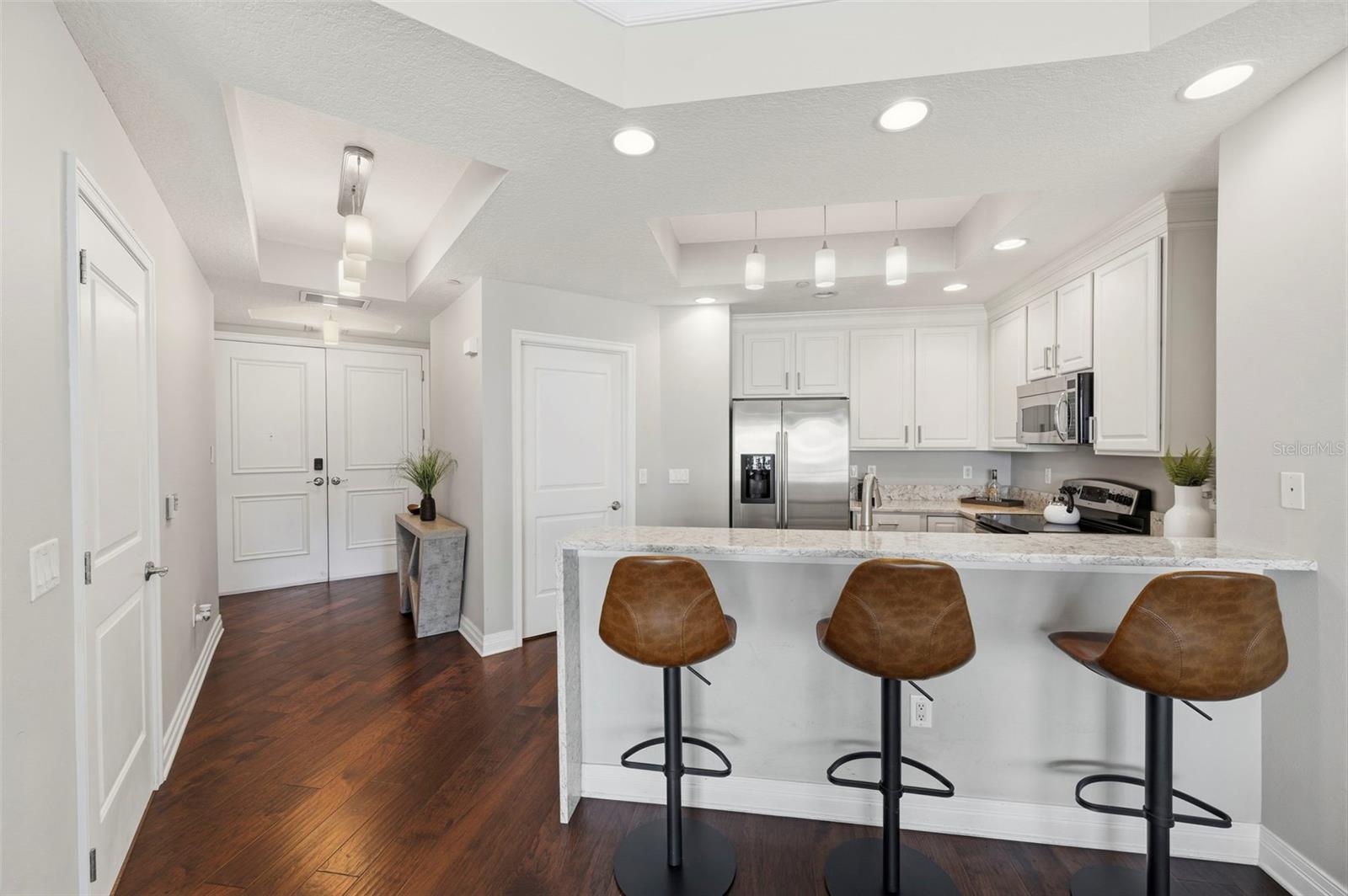 Condo kitchen with white cabinets, stainless steel appliances, and a granite island with three brown stools.