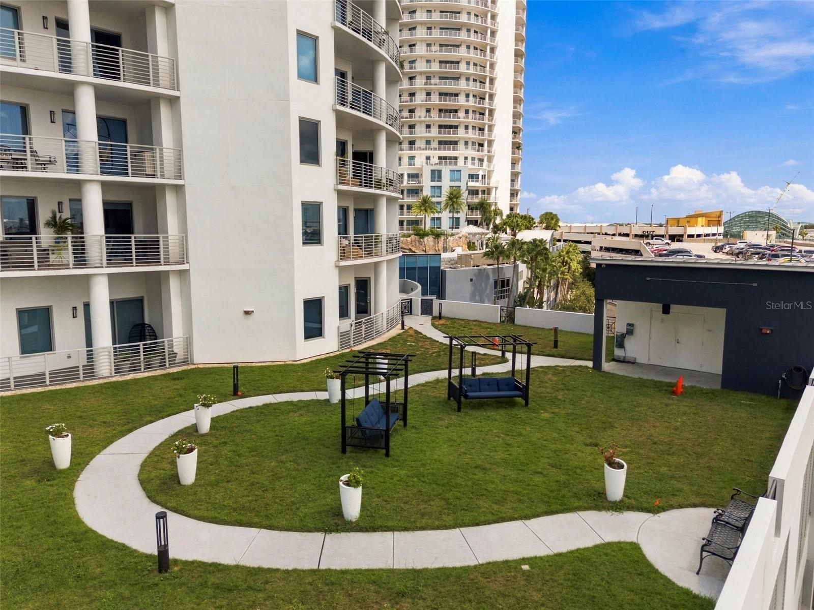 Condominium courtyard with a landscaped lawn, curved walkways, and swing seating.