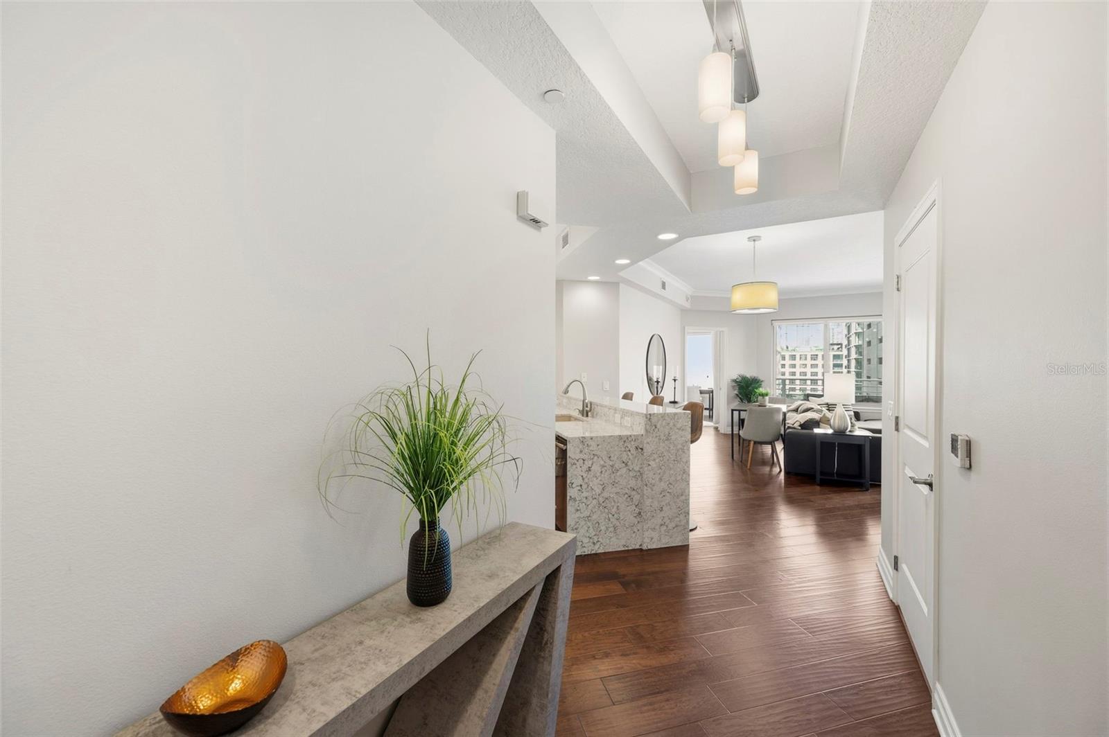 Condo entry hallway opening to a staged kitchen, dining area, and living room with city views.
