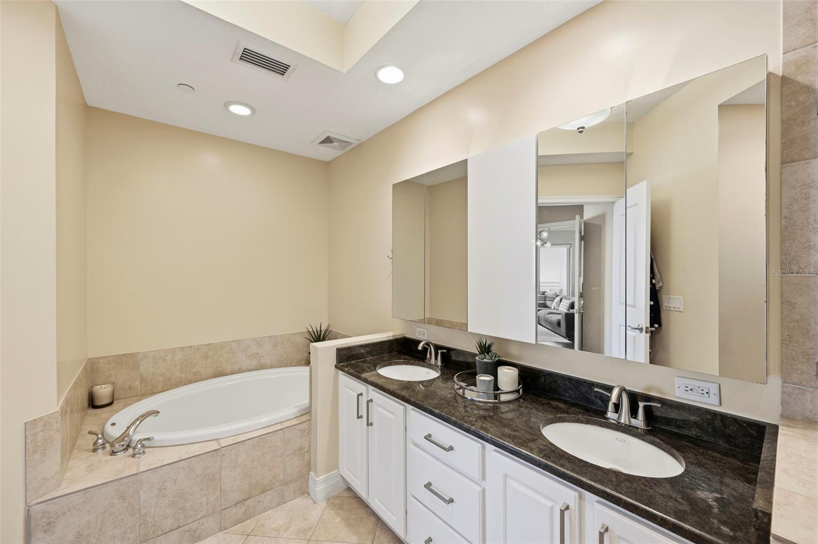 Bathroom with a corner soaking tub and long double vanity with dark stone countertop.
