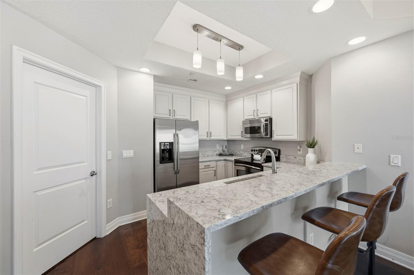 Condominium kitchen with white cabinets, stainless appliances, and a granite breakfast bar with leather stools.