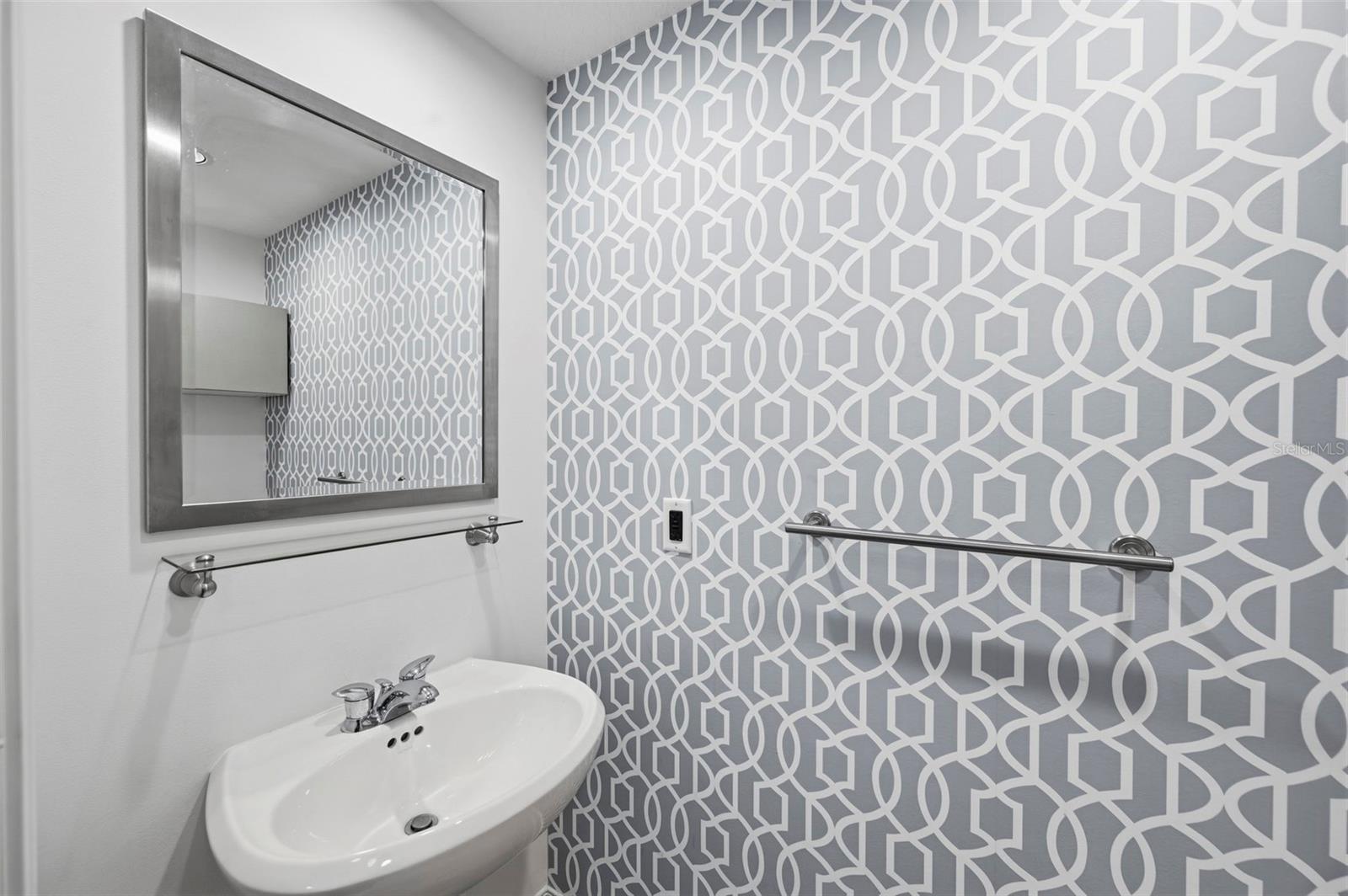 Bathroom vanity with white sink, metal-framed mirror, and geometric gray-and-white accent wall.