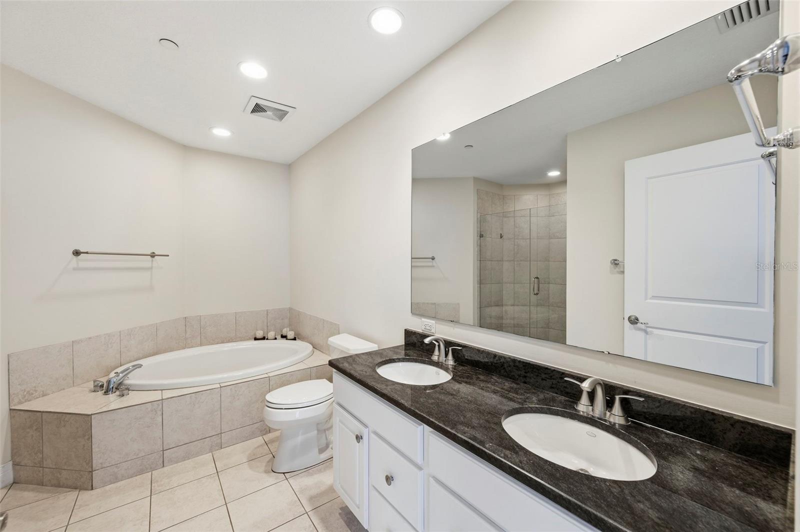 Bathroom with a built-in soaking tub, glass shower, and double-sink dark stone vanity.