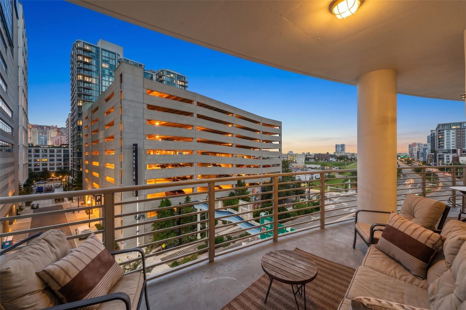 Condo balcony with cushioned seating and a city view at dusk.