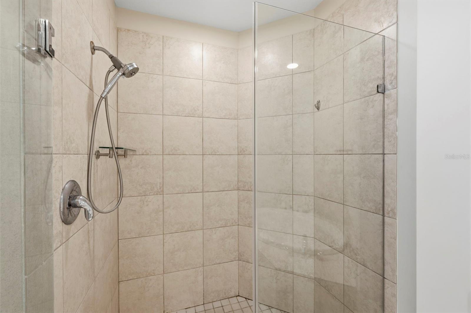 Tiled walk-in shower with a glass enclosure and handheld showerhead.