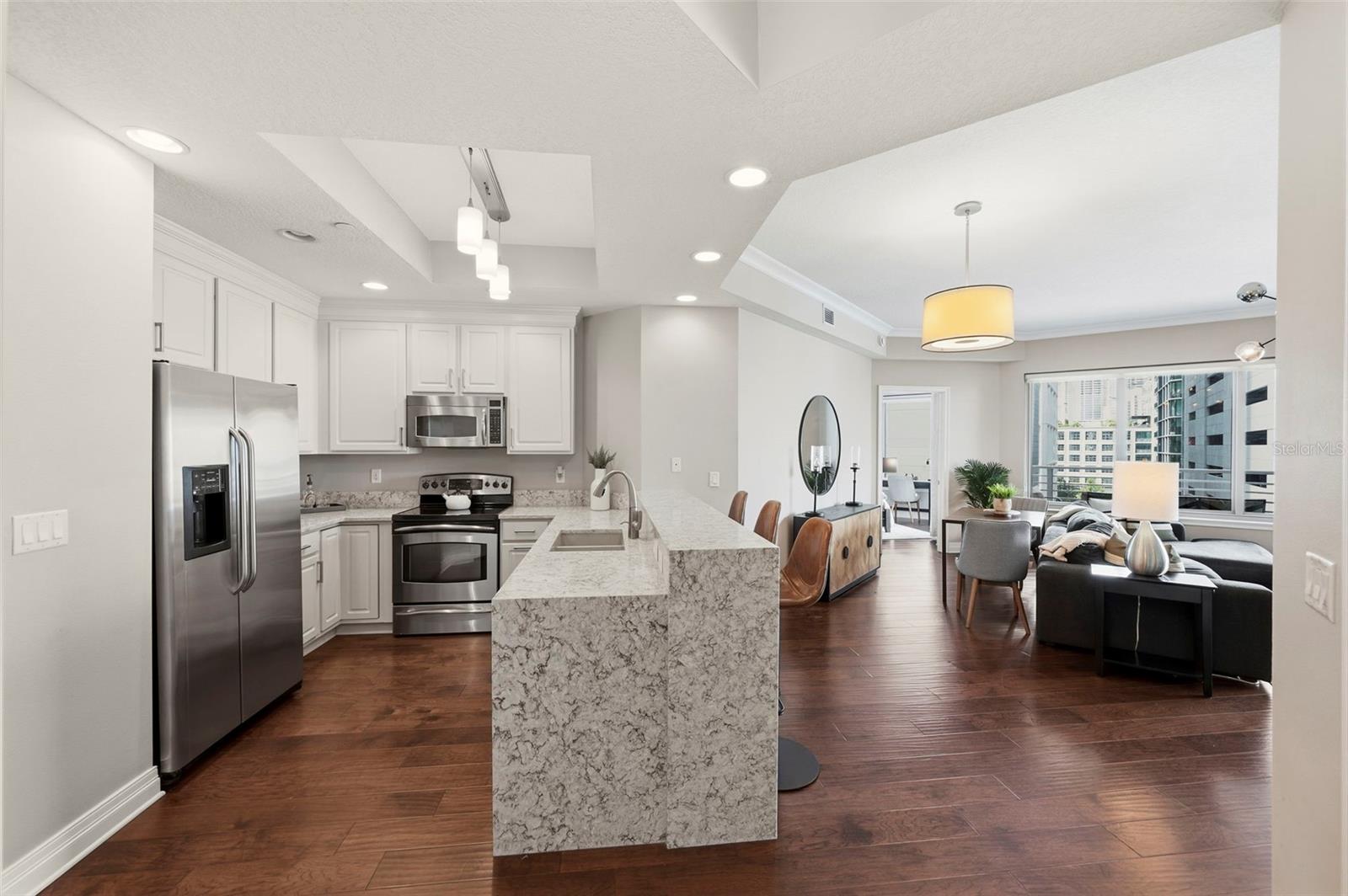 Open condo kitchen and living area with a granite island, dark wood floors, and city views.