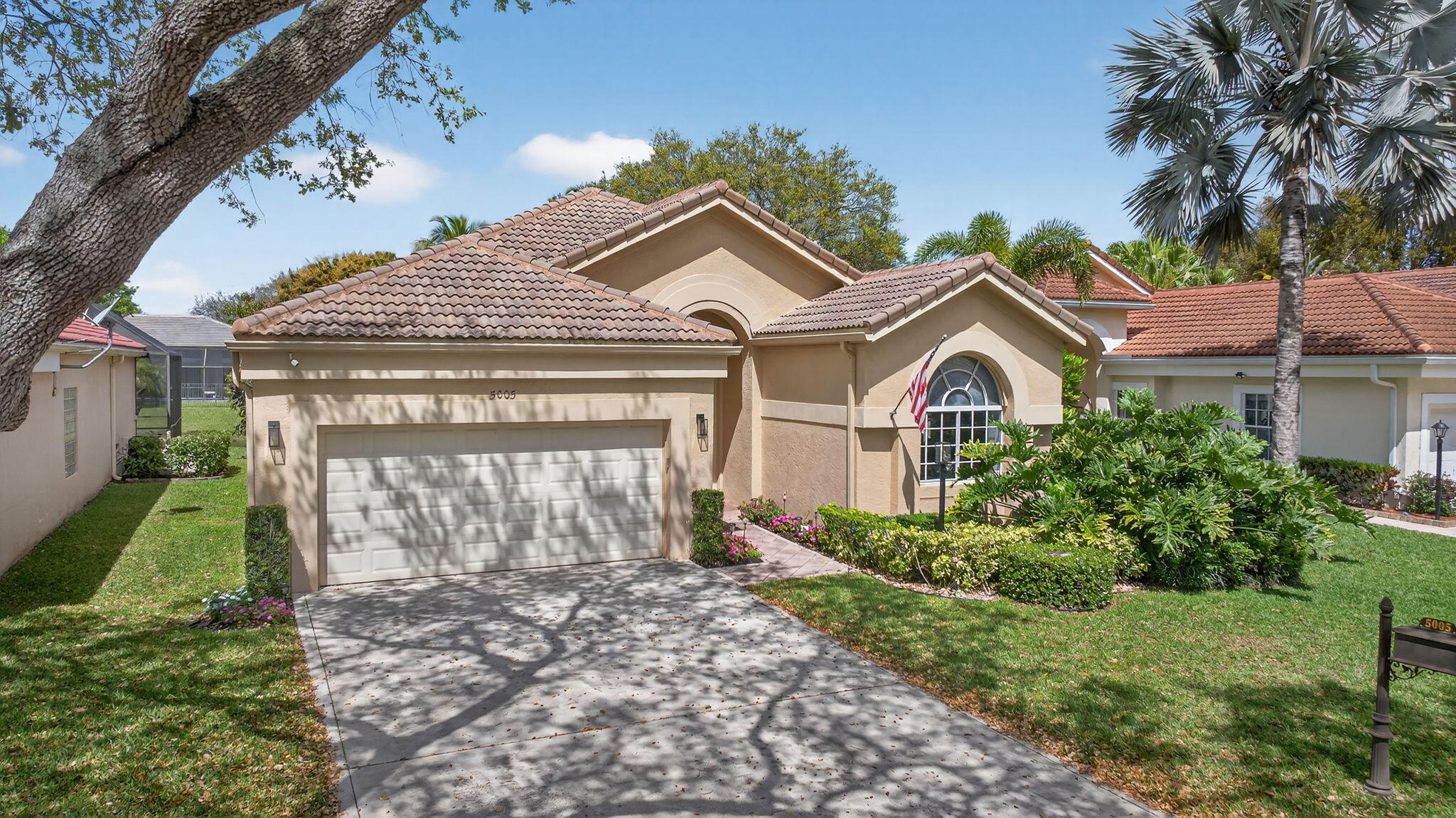 Beige home with a tile roof, double garage, arched window, and landscaped front yard.