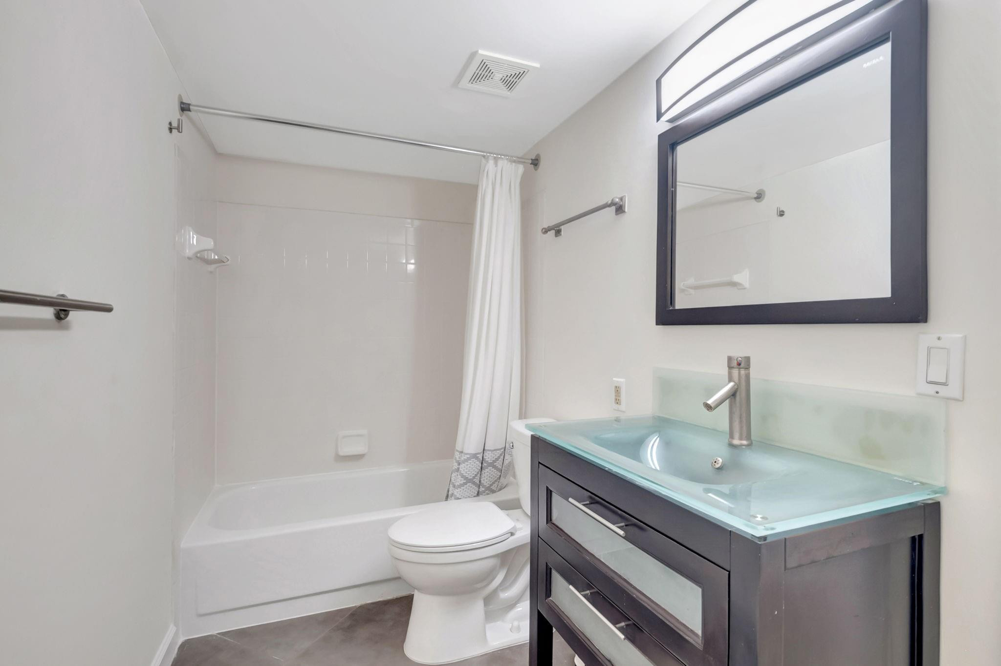 Bathroom with a white tub and shower, toilet, and dark vanity with a pale blue glass sink.