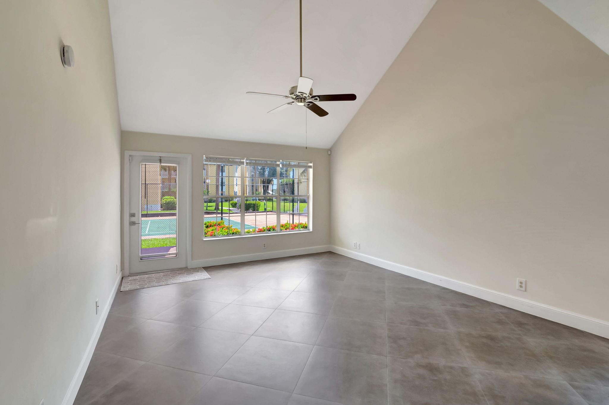 Empty tiled living room with a vaulted ceiling and views of a pool through the window and glass door.