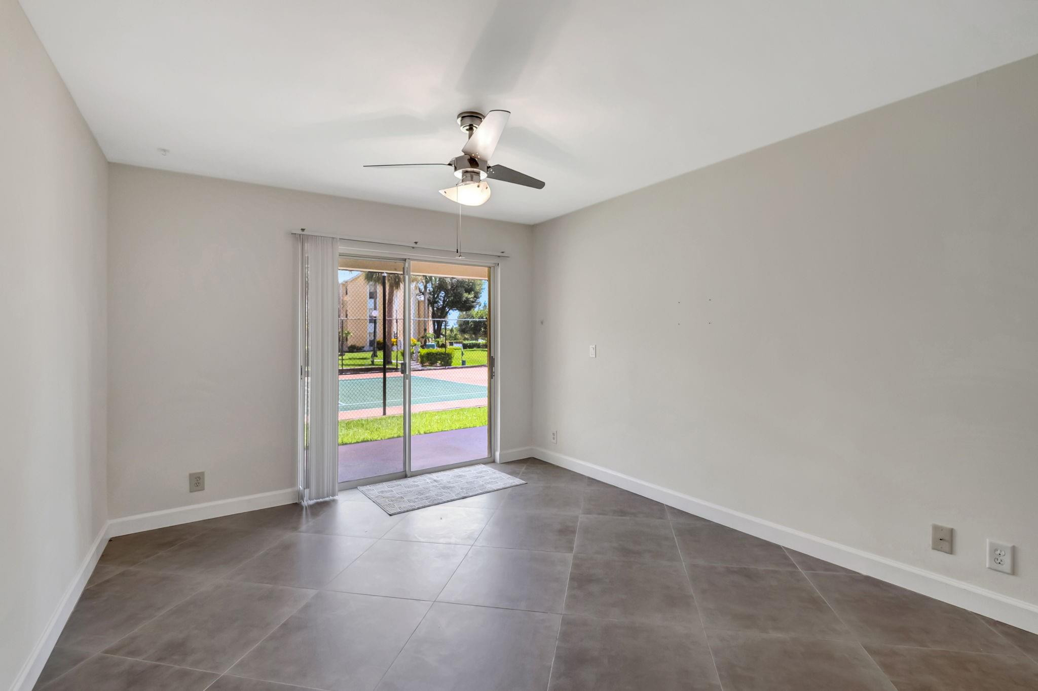 Empty tiled room with a ceiling fan and sliding glass doors opening onto a patio.