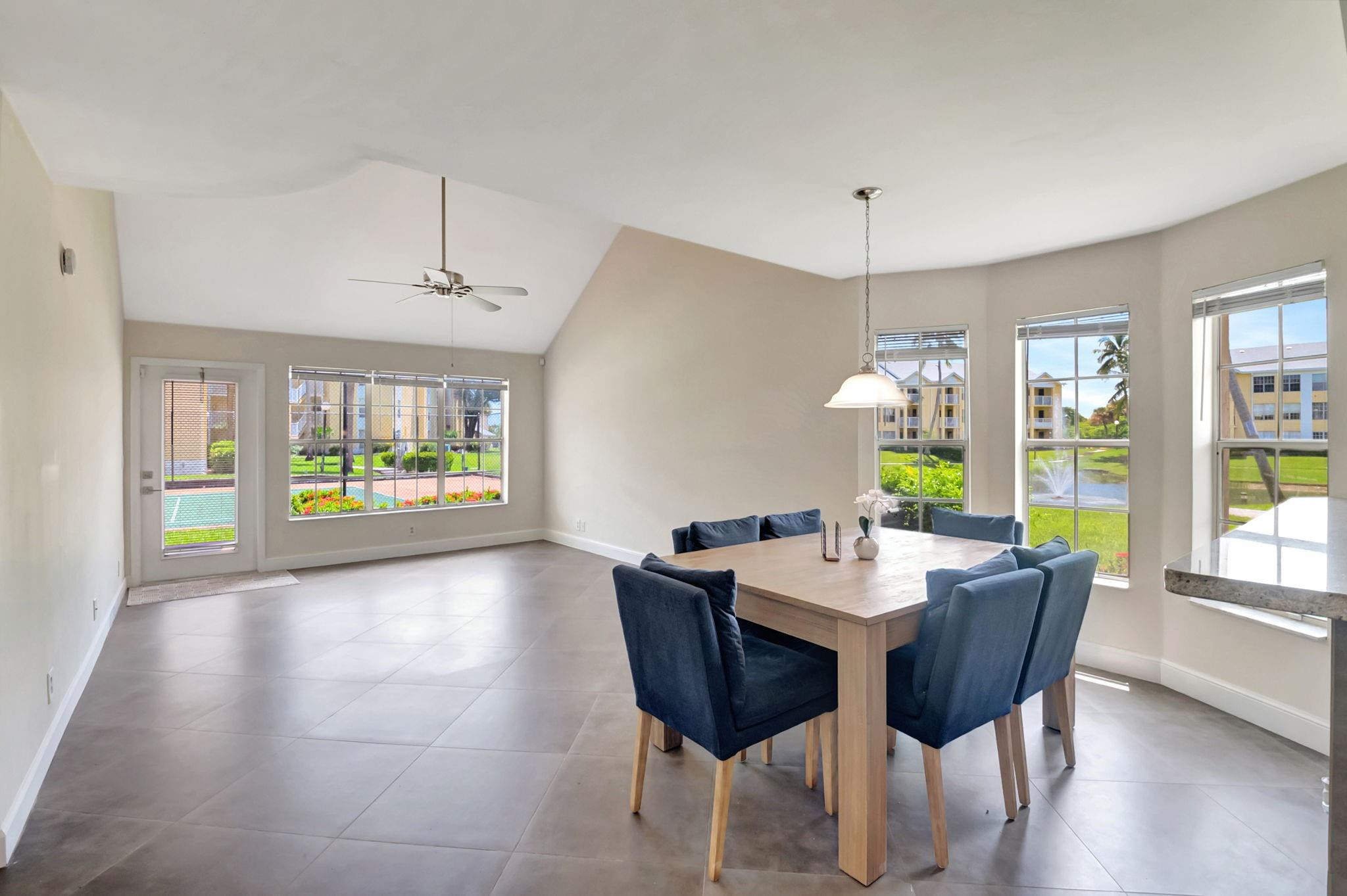 Dining area with a wood table, navy chairs, vaulted ceiling, and large windows overlooking a landscaped courtyard.